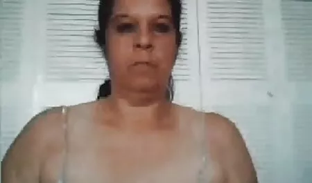 Seorang wanita dengan rambut coklat di kaca di baju hitam, akak seks meletakkan tangannya di pantat di depan kamera.